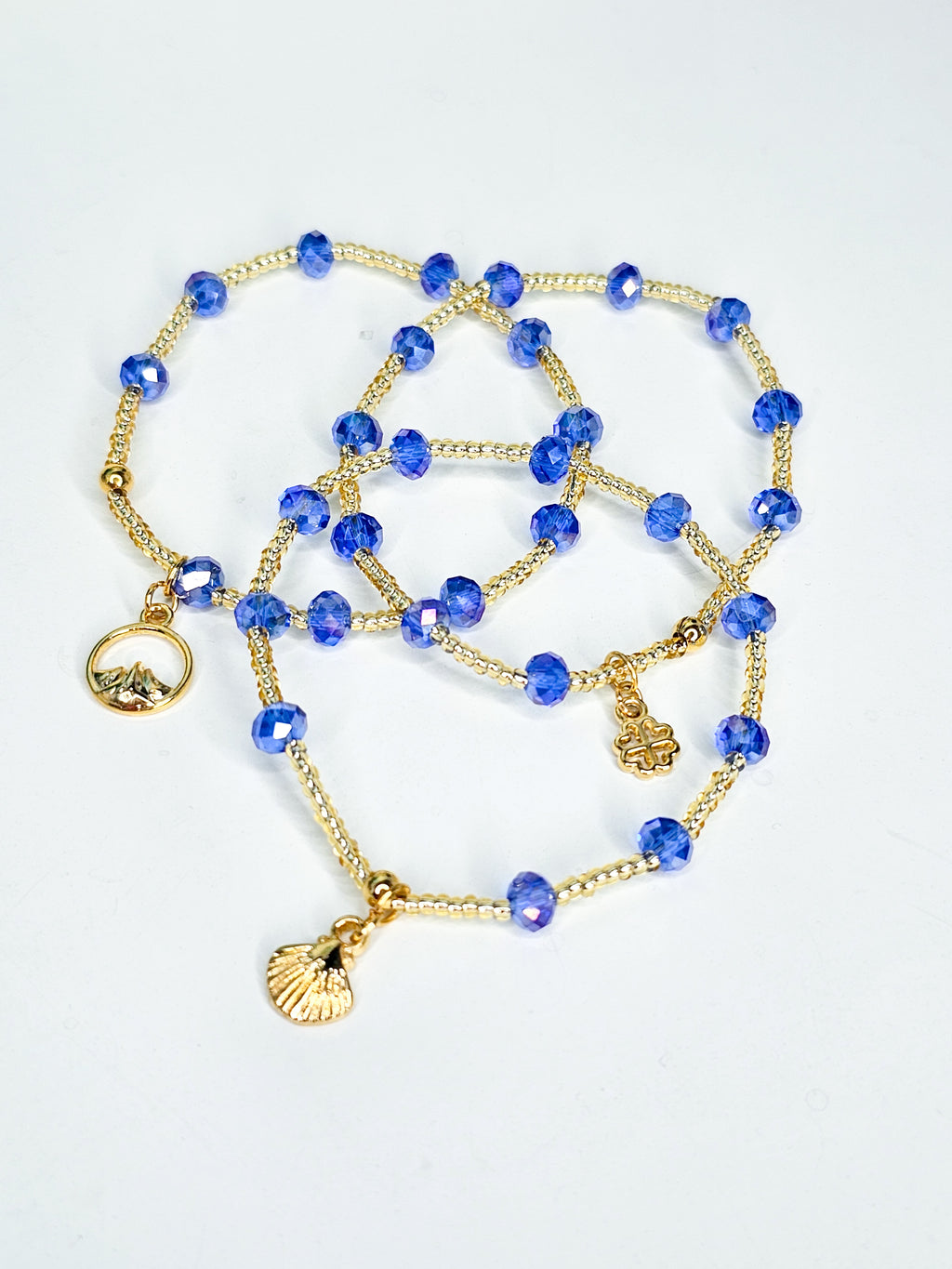 Gold and blue beaded bracelet with charms on a light gray background