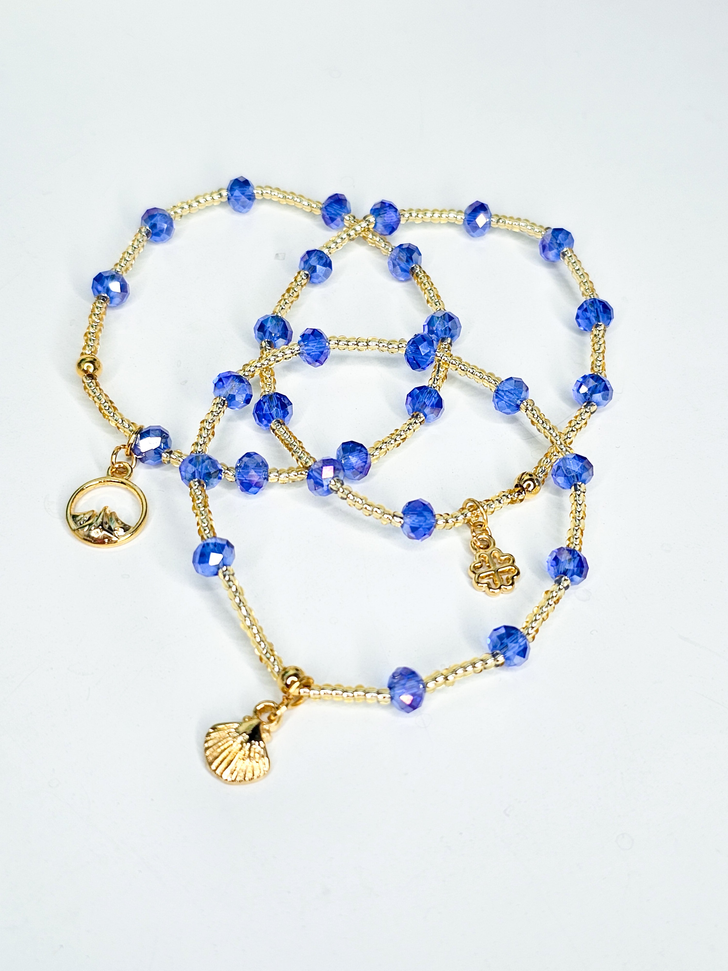 Gold and blue beaded bracelet with charms on a light gray background